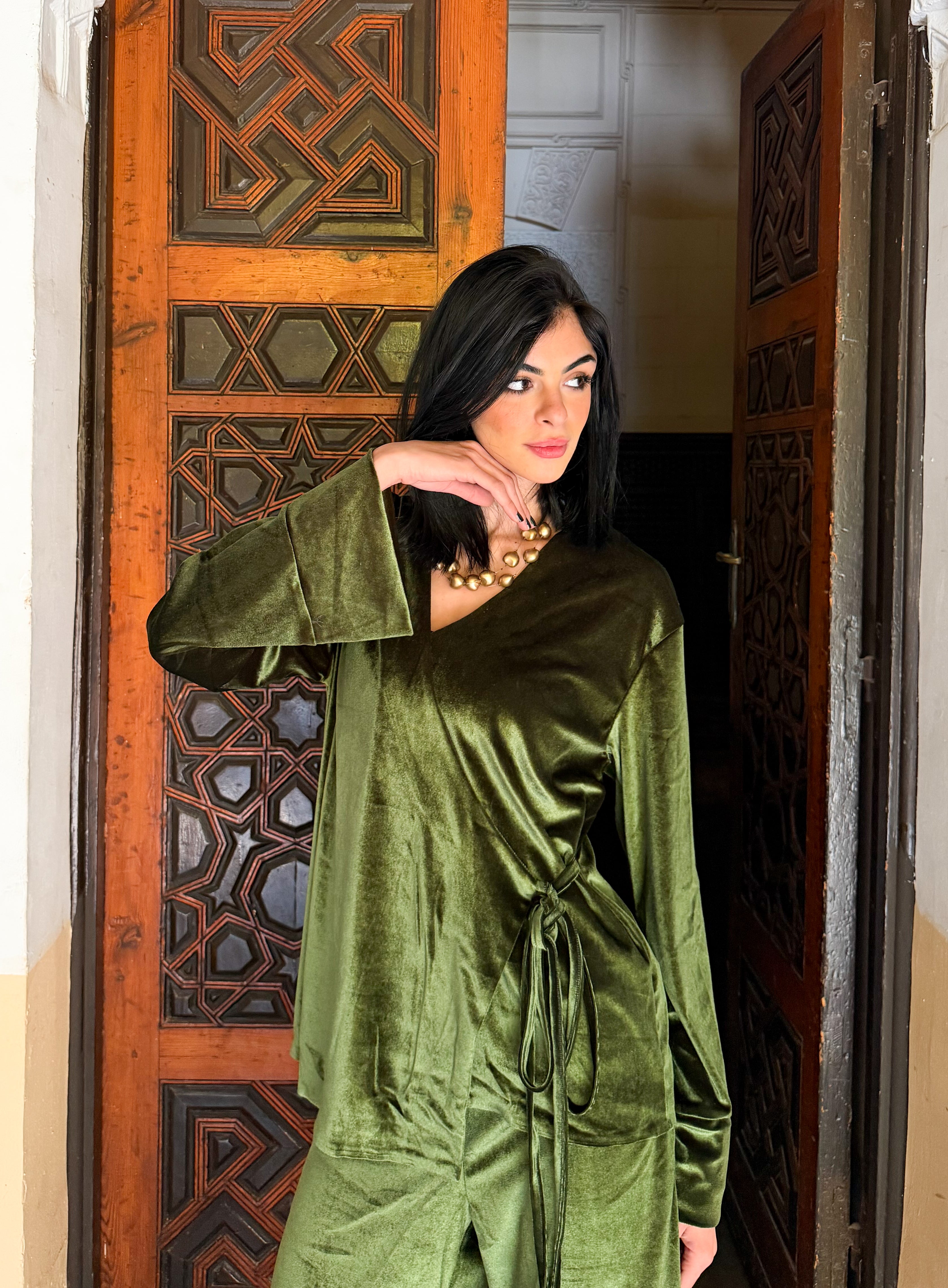 Woman wearing a green velvet outfit standing in front of an ornate wooden door.